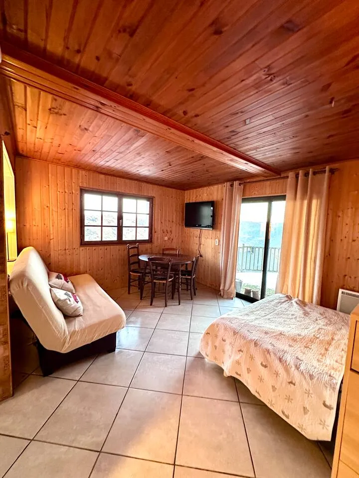 Coin nuit et espace repas en bois de La Marmotte, avec le balcon au fond.